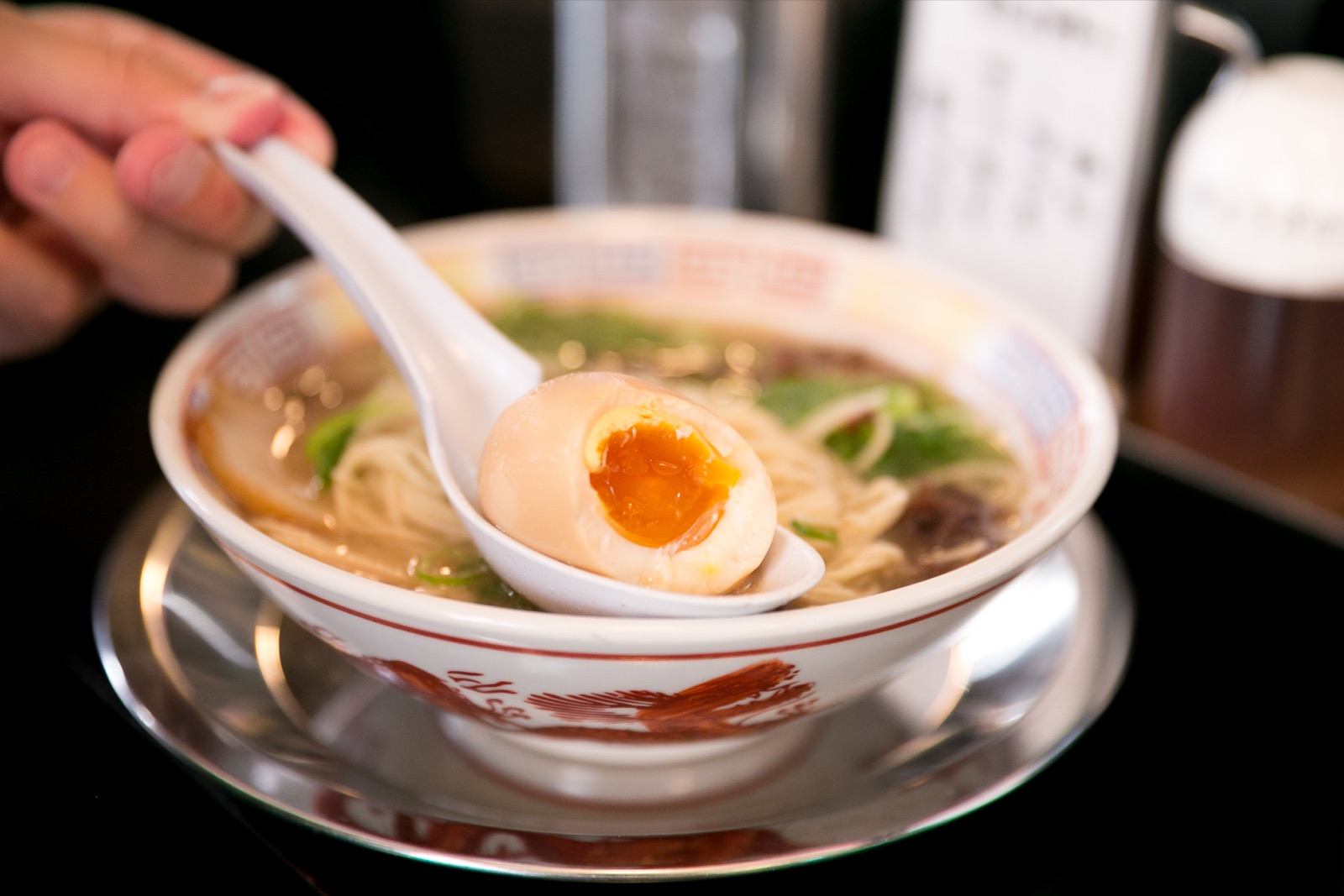 Bol de ramen japonais avec nouilles, bouillon clair et un oeuf mollet mariné au jaune coulant posé sur une cuillère
