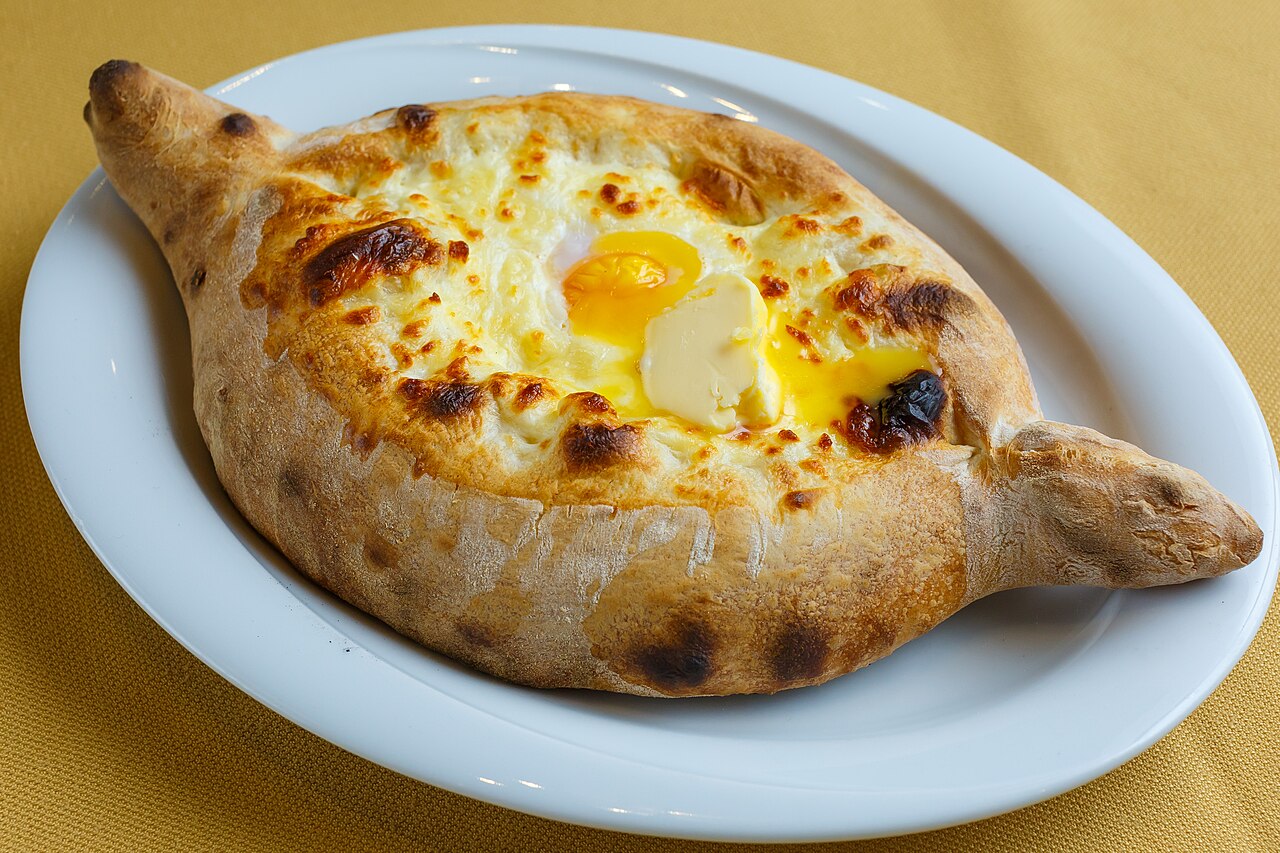 Khachapuri adjarien en forme de barque, garni de fromage fondu, d'un jaune d'œuf et d'une noix de beurre, servi dans une assiette blanche