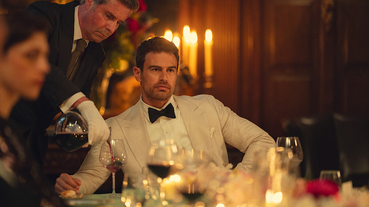 Theo James en smoking blanc à un dîner aux chandelles, un serveur lui versant du vin, dans la saison 2 de The Gentlemen