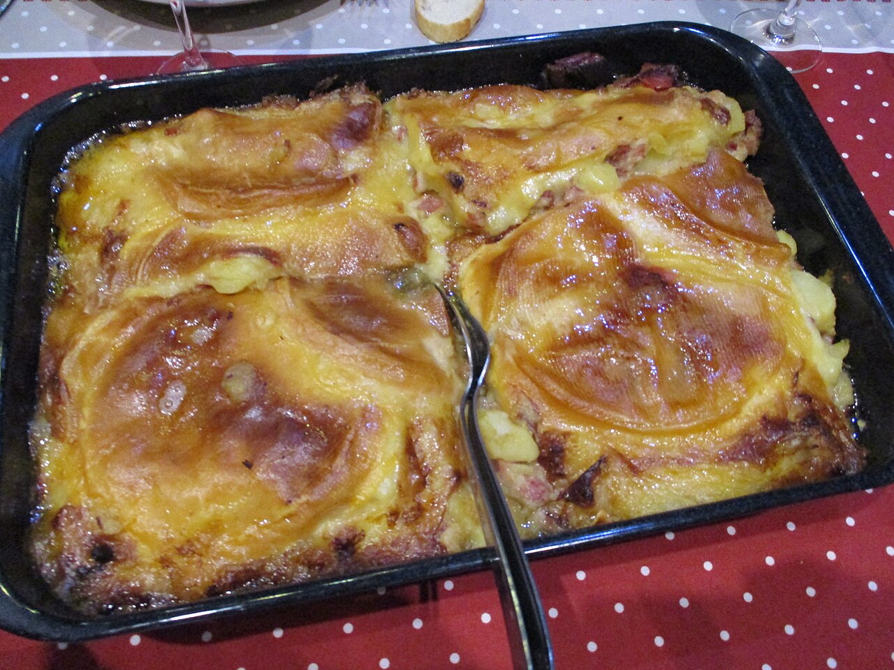 Une tartiflette dorée au reblochon fondu, lardons et pommes de terre, servie dans un plat noir