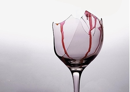 Verre à vin brisé taché de vin rouge sur fond clair, ambiance d'un dîner qui tourne mal