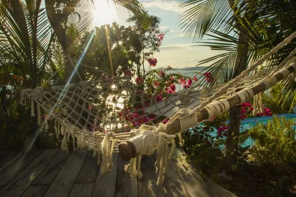 Hamac en corde tendu entre des palmiers au soleil, invitant à la sieste l'après-midi