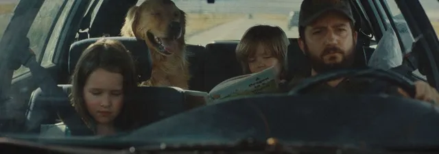 Un père au volant d'une vieille voiture avec ses deux enfants et un golden retriever, sur une route du Midwest, dans le film Sur la route d'Omaha