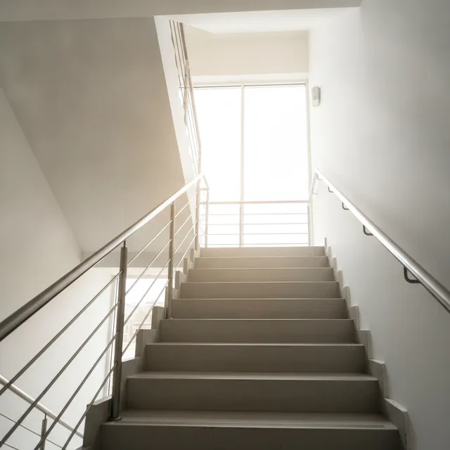 Cage d'escalier lumineuse vue de bas en haut, marches claires et rampe metallique