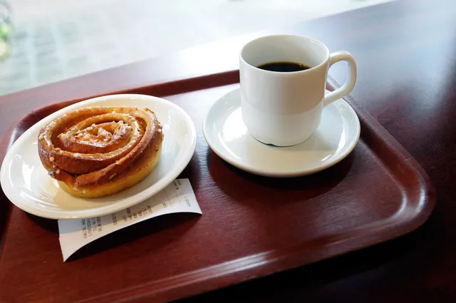 Un kanelbulle sur une assiette et une tasse de cafe noir sur un plateau, dans un cafe suedois