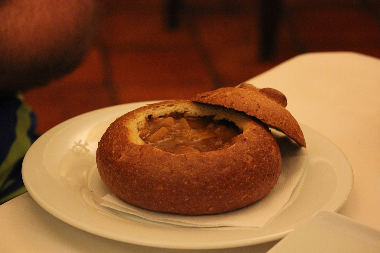 Soupe goulash servie dans une miche de pain évidée, sur une assiette blanche