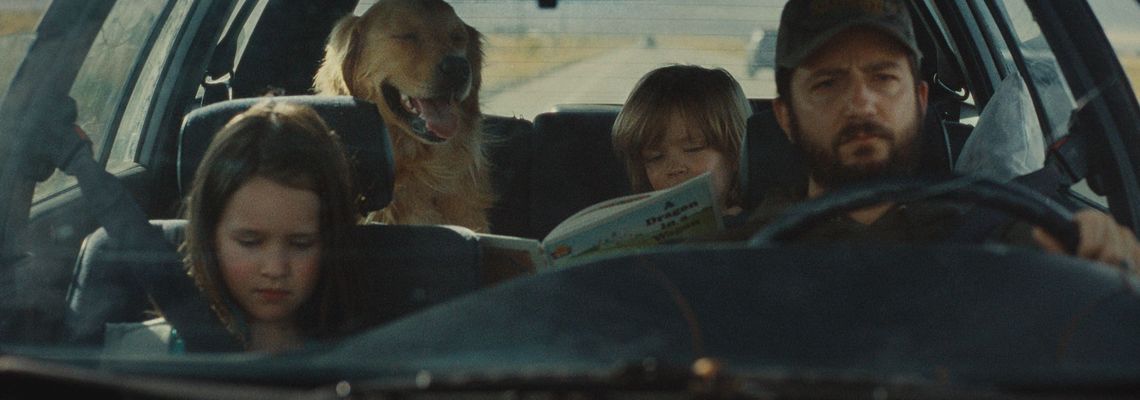 Un père au volant d'une vieille voiture avec ses deux enfants et un golden retriever, sur une route du Midwest, dans le film Sur la route d'Omaha